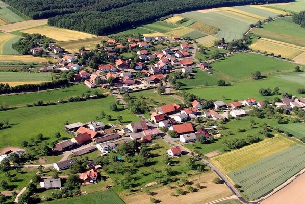 Ett flygbildsbild av en lantlig by med hus som ligger tätt tillsammans runt ett centralt område, omgivet av åkrar.
