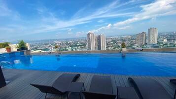 A rooftop swimming pool with lounge chairs and a cityscape view.