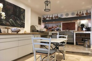 A kitchen with white cabinetry, a dining table with chairs, and a hanging pot rack above the stove. - Holiday home in Le Barroux with Wi-Fi (Le Barroux)