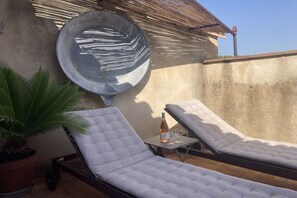 A rooftop terrace with two lounge chairs, a potted plant, a table with a bottle and glasses, and a decorative wall plate. - Holiday home in Le Barroux with Wi-Fi (Le Barroux)