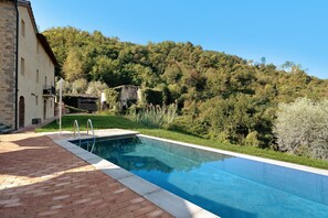A swimming pool with a brick pathway leading to it, surrounded by lush greenery and a hillside. - Holiday Home 'Villa Roncacccio' with Mountain View, Wi-Fi and Air Conditioning (Borgo a Mozzano)