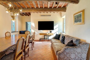A dining area with a wooden table and chairs, a flat-screen TV mounted on the wall, and a patterned sofa. - Holiday Home 'Villa Roncacccio' with Mountain View, Wi-Fi and Air Conditioning (Borgo a Mozzano)