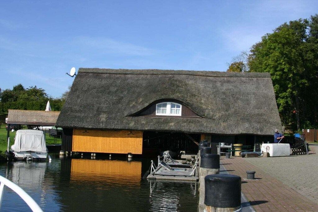 A thatched-roof building with a dock extending into a body of water, a satellite dish on the roof, and a person working near the dock.