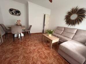 Un salon comprenant un canapé, une table basse, une table à manger avec des chaises et un élément décoratif mural.