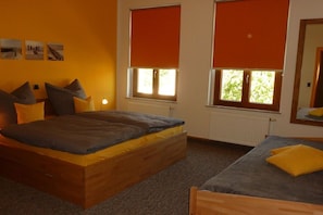 A bedroom with a wooden bed, a smaller bed, and two windows with orange blinds. - A2 in the apartment building near Müritz (Waren (Müritz))