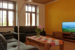 A living room with a sofa, a coffee table, a TV, and a window with blinds. - A2 in the apartment building near Müritz (Waren (Müritz))
