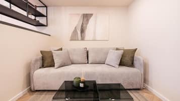 Ein modernes Wohnzimmer mit einem grauen Sofa, einem Glastisch und einem minimalistischen Gemälde an der Wand.