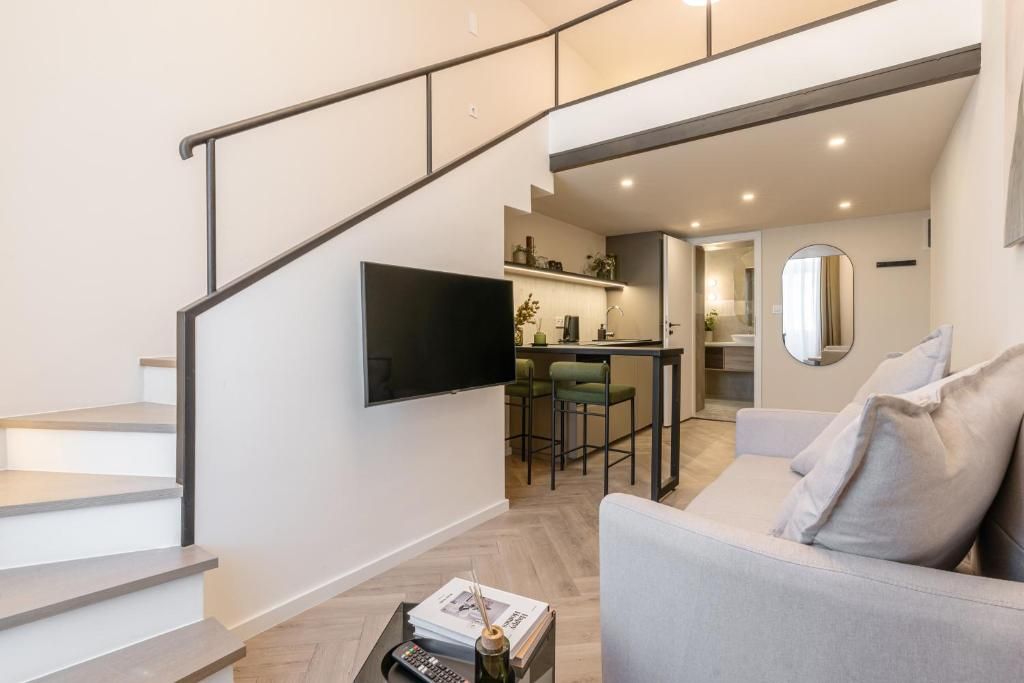 Ein moderner Wohnraum mit Treppe, einem an der Wand befestigten Flachbildfernseher, einer Essecke mit Barhocker und einer Couch mit Kissen.