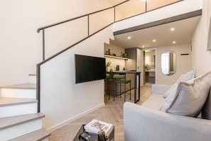 Ein moderner Wohnraum mit Treppe, einem an der Wand befestigten Flachbildfernseher, einer Essecke mit Barhocker und einer Couch mit Kissen.