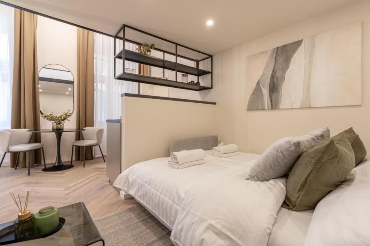 Ein modernes Hotelzimmer mit einem Bett, einer Sitzecke mit Stühlen, einem kleinen Tisch und einem an der Wand befestigten Regal.