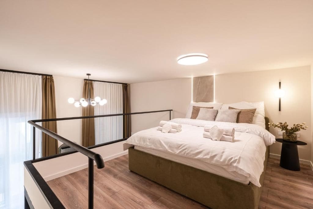 Ein modernes Schlafzimmer mit einem großen Bett, einem Nachttisch, einer Zimmerpflanze und einer Treppe mit Geländer.