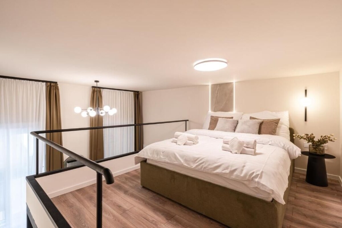 Ein modernes Schlafzimmer mit einem großen Bett, einem Nachttisch, einer Zimmerpflanze und einer Treppe mit Geländer.