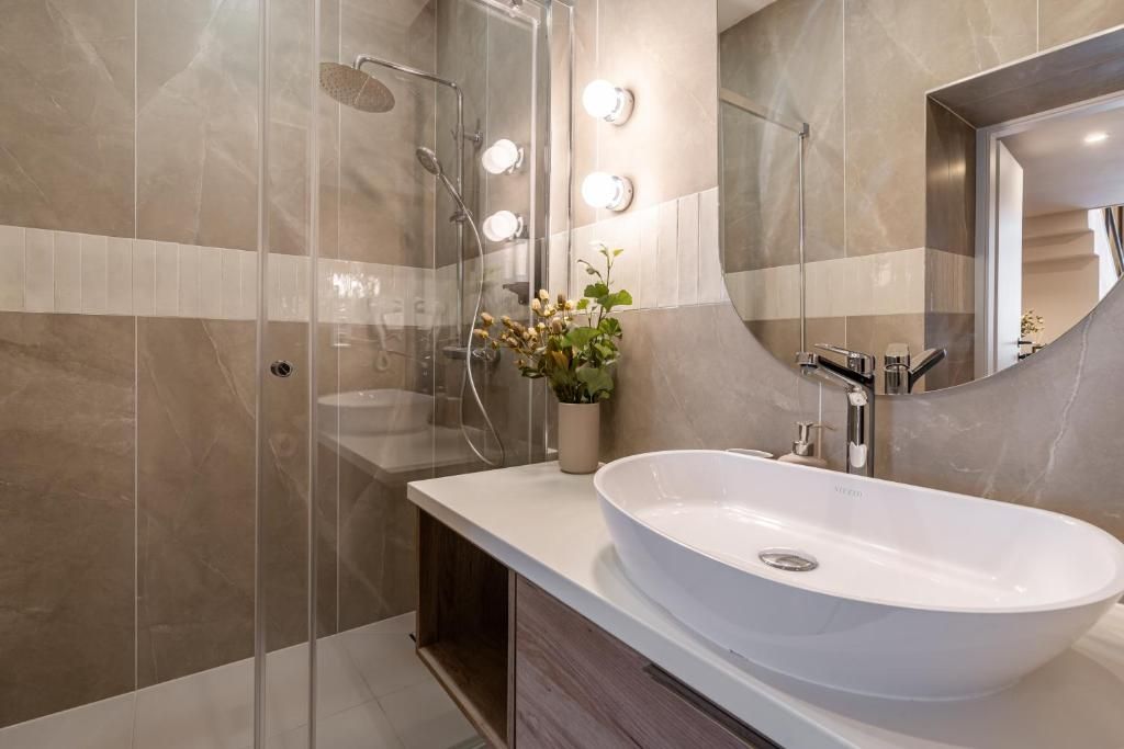 Ein modernes Badezimmer mit einem großen weißen Waschbecken, einer Duschkabine aus Glas und einem beleuchteten Spiegel.