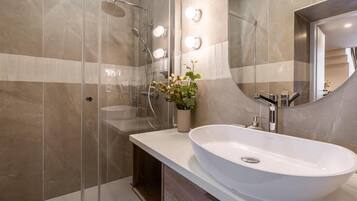 Ein modernes Badezimmer mit einem großen weißen Waschbecken, einer Duschkabine aus Glas und einem beleuchteten Spiegel.