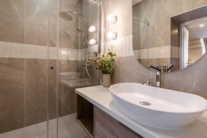 Ein modernes Badezimmer mit einem großen weißen Waschbecken, einer Duschkabine aus Glas und einem beleuchteten Spiegel.