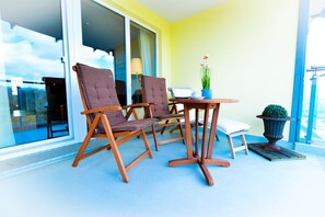 Ein Balkon mit zwei Holzschaukelstühlen, einem kleinen Tisch mit einer Topfpflanze und Blick zum Himmel durch große Fenster.