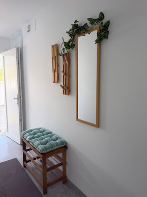 A hallway with a wooden bench, a mirror, and a wall-mounted plant. - Vacation Apartment (Vejer de la Frontera)