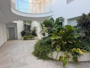 A spacious indoor courtyard with a tiled floor, surrounded by various potted plants and a balcony railing. - Vacation Apartment (Vejer de la Frontera)