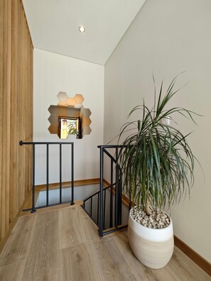 A wooden staircase with a black railing, a potted plant, and a wall-mounted light fixture.