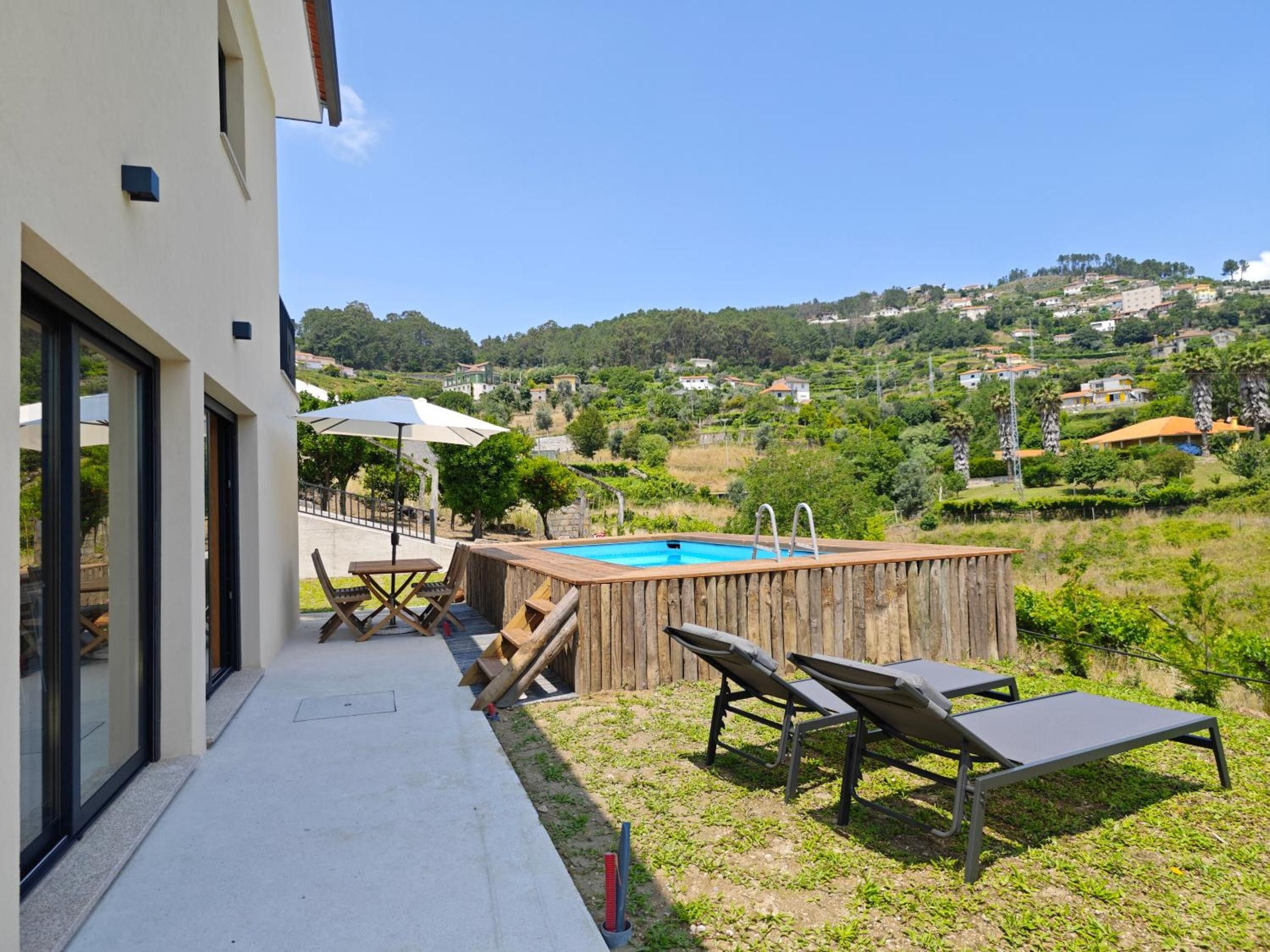 A modern outdoor pool area with lounge chairs and a wooden deck, overlooking a hilly landscape.