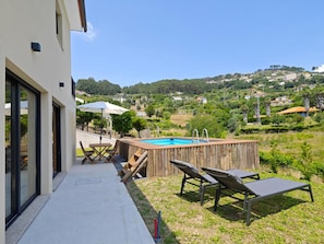 Un área de piscina moderna al aire libre con sillones de descanso y una terraza de madera, con vistas a un paisaje montañoso.