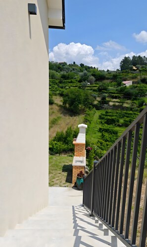 Een trap die leidt naar een balkon met uitzicht op een weelderige tuin, een bakstenen schoorsteen en een gootsteen.