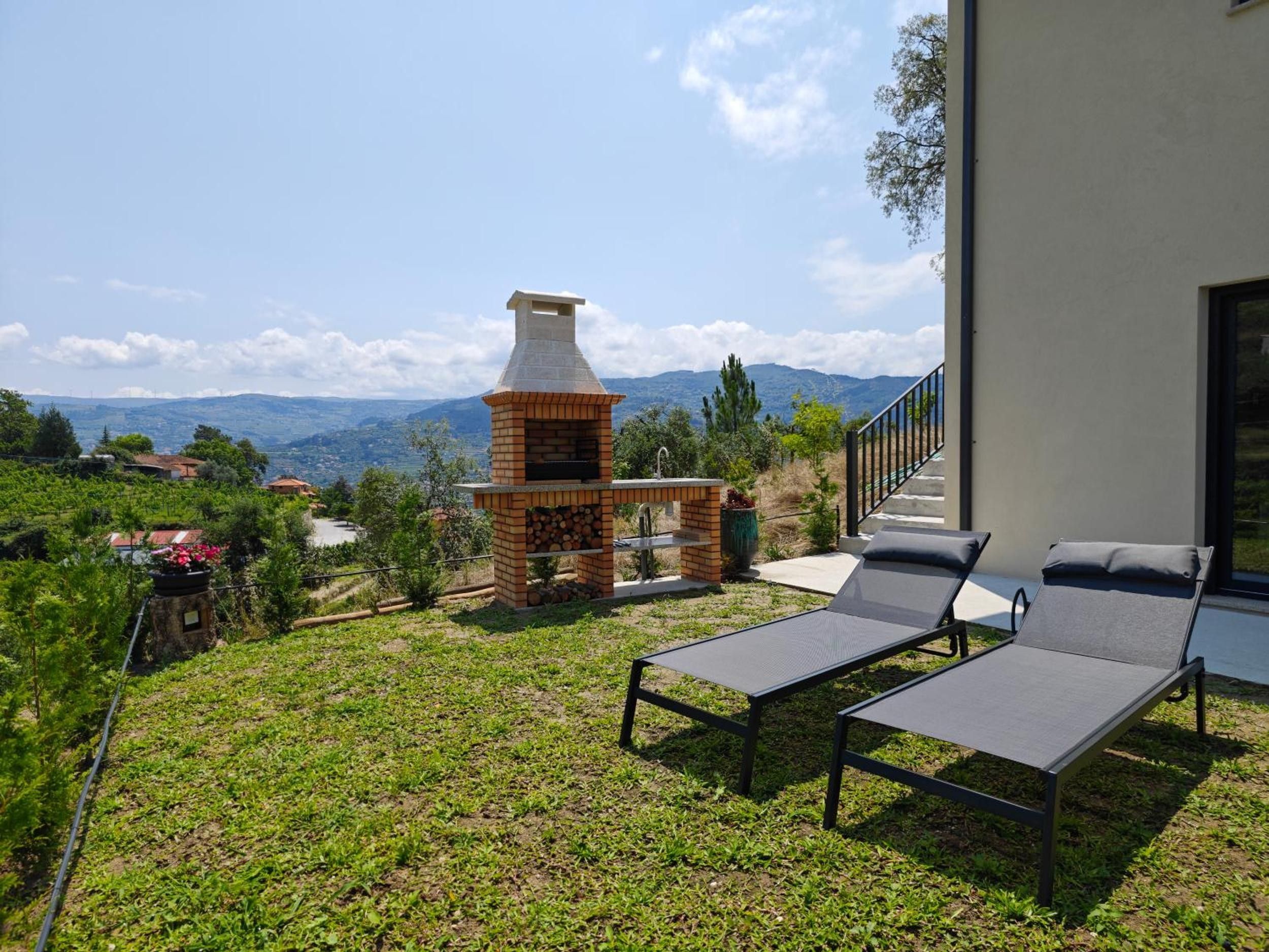 A patio with two lounge chairs, a brick barbecue grill, and a view of the mountains.