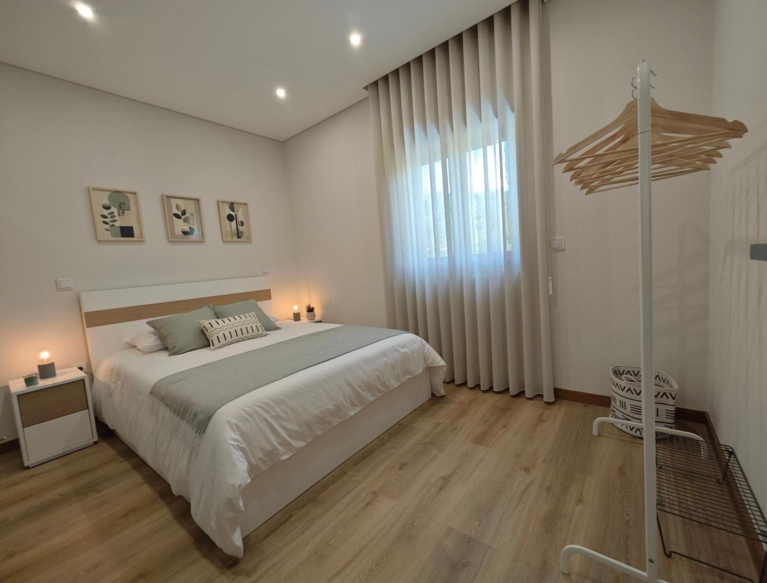 A bedroom with a bed, bedside tables, a hanging rack, and a window with curtains.