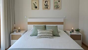 Een net opgemaakt bed met twee kussens, een nachtkastje met een lamp, en drie ingelijste kunstwerken aan de muur.