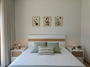 Una cama bien hecha con dos almohadas, una mesita de noche con una lámpara y tres obras de arte enmarcadas en la pared.