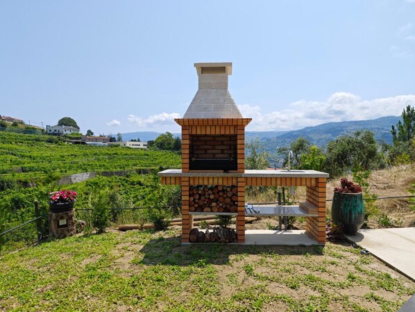 Una parrilla de ladrillo para barbacoa al aire libre con una chimenea, frente a un viñedo.