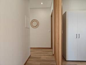 A hallway with wooden flooring, a white wardrobe, and a wall-mounted circular mirror.