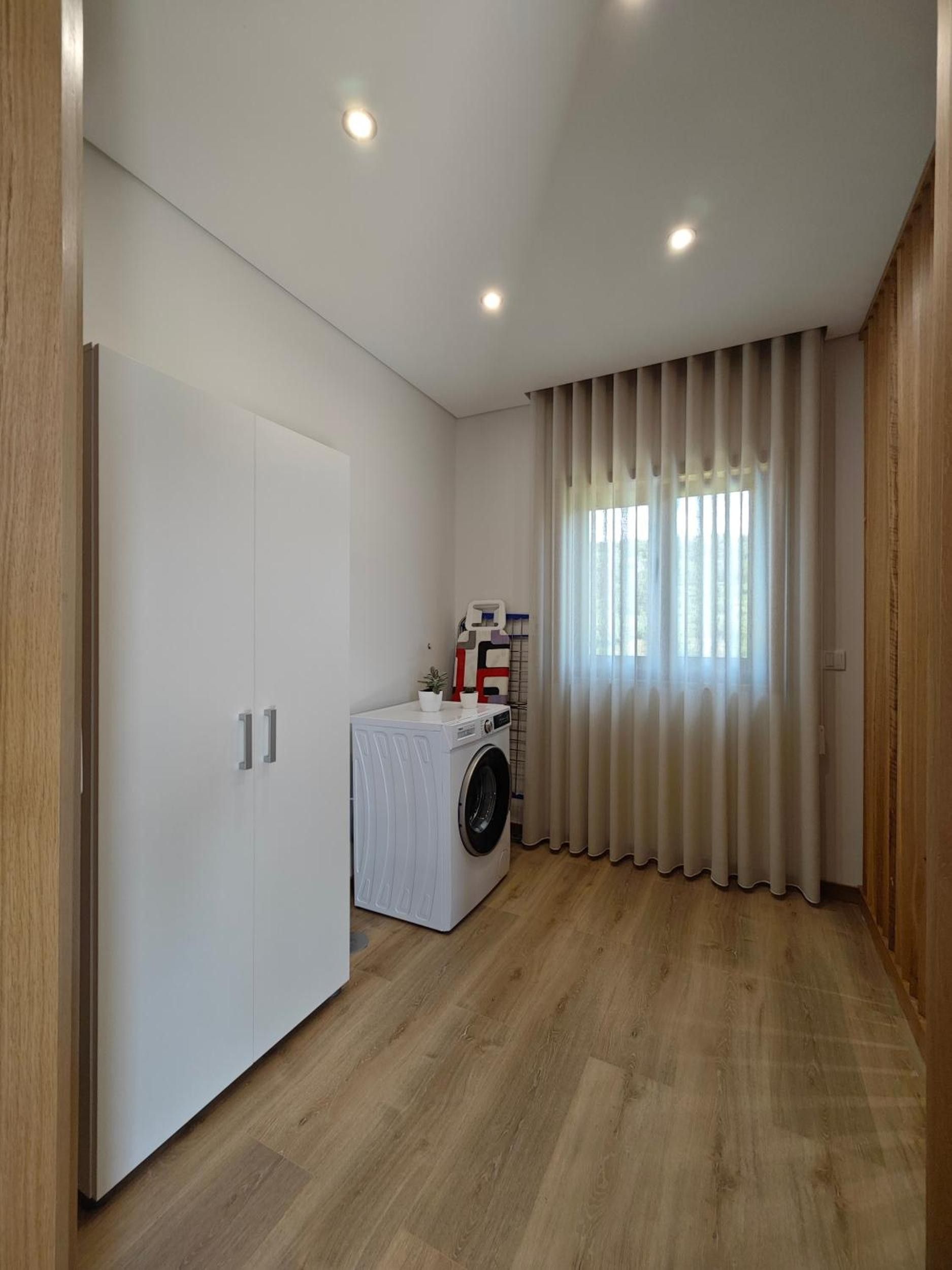 A compact room with a washing machine, a wardrobe, and a window with curtains.
