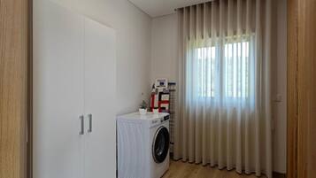 A compact room with a washing machine, a wardrobe, and a window with curtains.