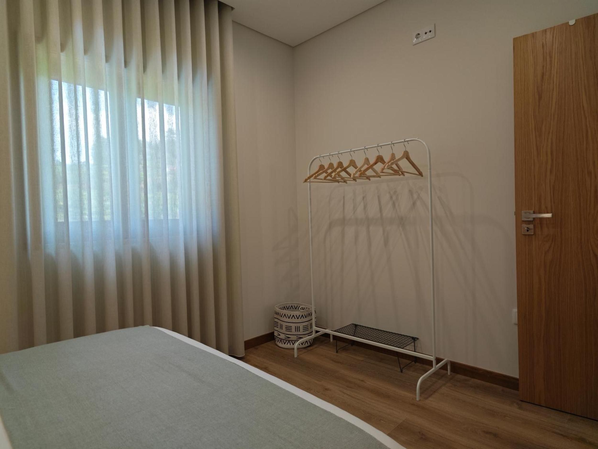 A bedroom with a bed, a wooden door, a window with curtains, and a metal drying rack.