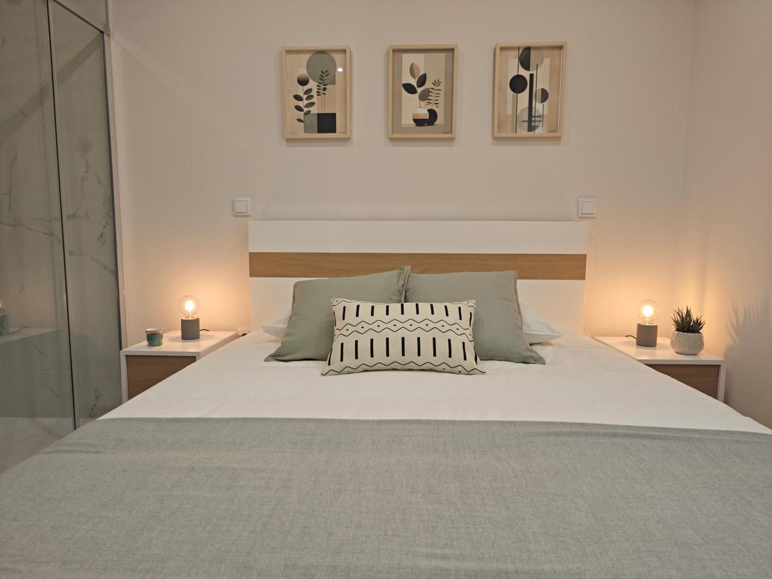 A modern bedroom with a large bed, two bedside tables, and three framed artworks on the wall.