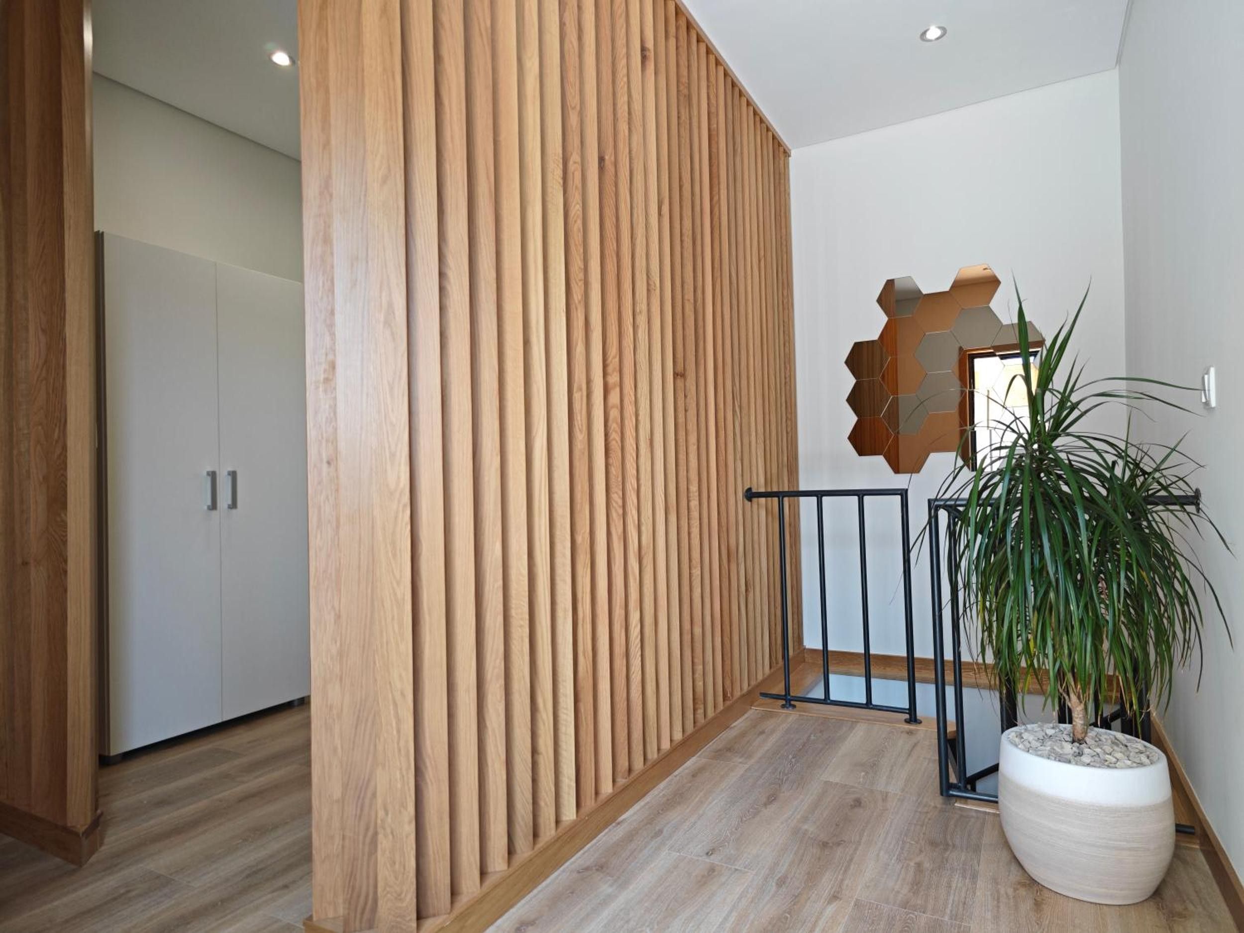 A hallway with a wooden slat wall, a potted plant, and a geometric wall decoration.