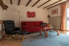 A living room with a red sofa, a black chair, a glass coffee table, and a blue rug. - Holiday apartment with 1 bedroom (Neunkirchen)