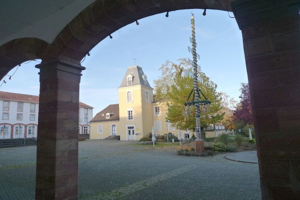 A courtyard with a yellow building, a bell tower, and a stone archway.