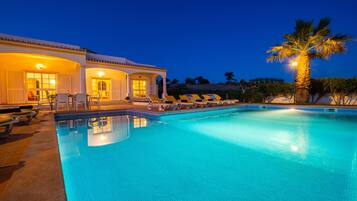 A swimming pool with lounge chairs and a building with lights.