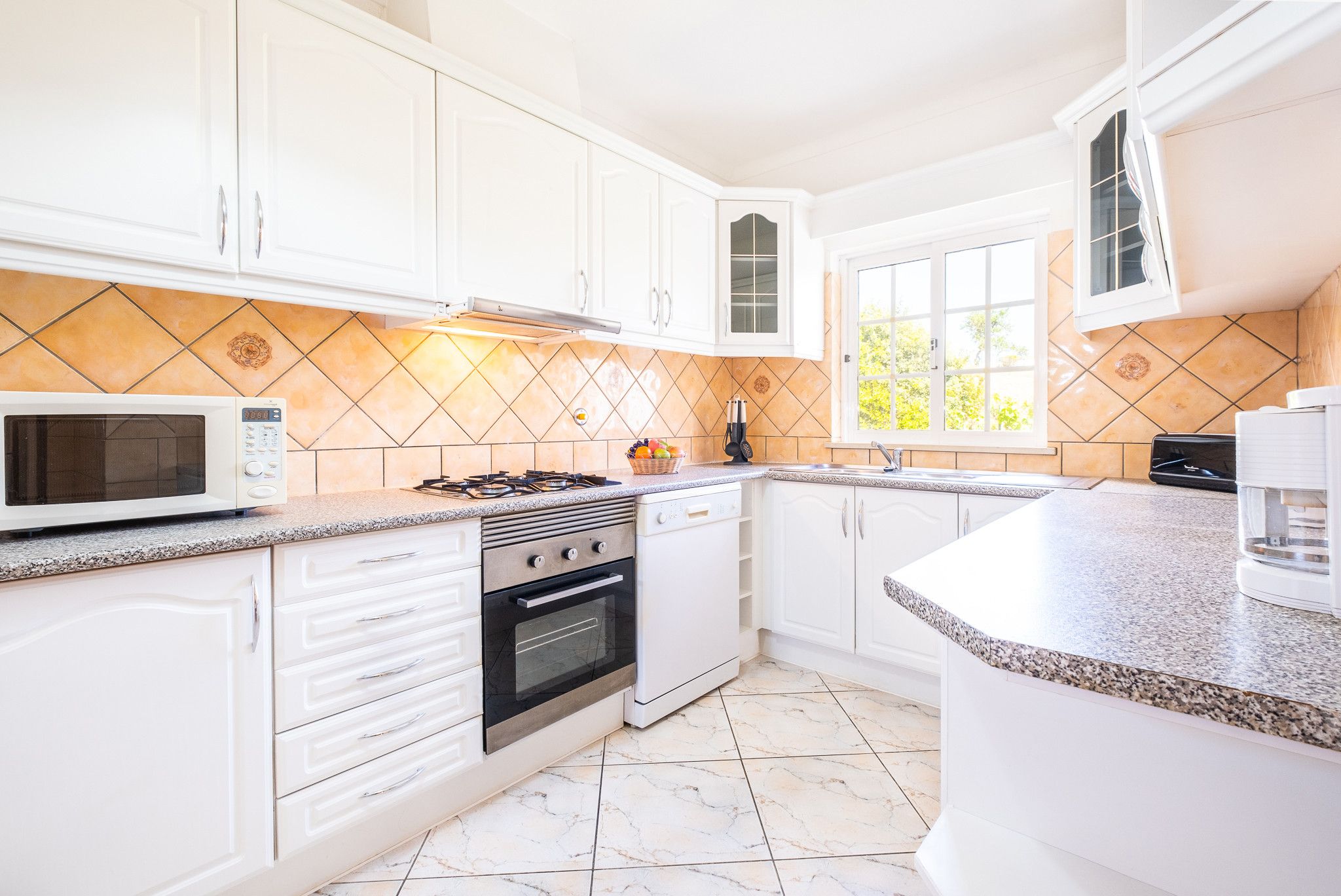 Une cuisine moderne avec des meubles blancs, un four à micro-ondes, une cuisinière et un évier.