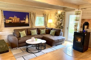 Ein gemütliches Wohnzimmer mit einem Ecksofa, einem Kamin, einem großen Fenster mit Vorhängen und einem gerahmten Bild eines Gebäudes.