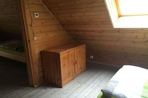 Ein Zimmer mit schrägen Wänden, Holzvertäfelung, einem kleinen Schrank und einem Bett mit einem gestreiften Kopfkissen.
