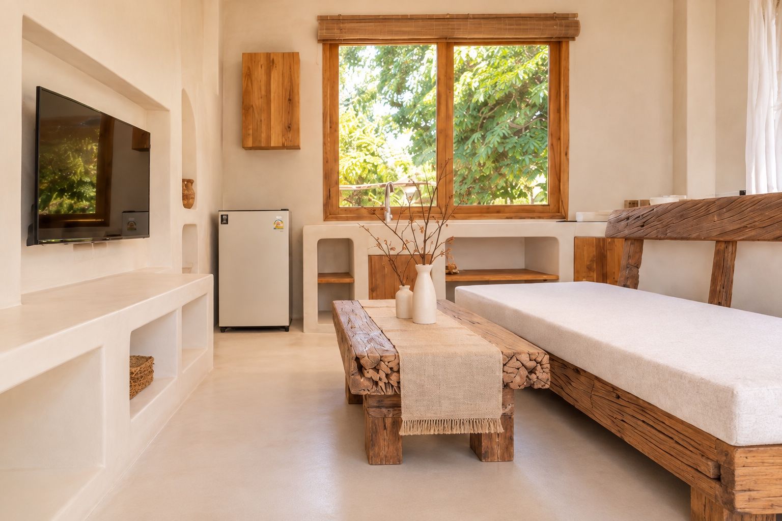 Una habitación con cama, televisión, refrigerador y ventana con vista a árboles.