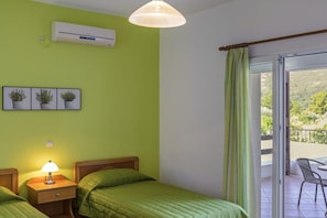 A room with two beds, a nightstand with a lamp, a wall-mounted air conditioner, and a view of a balcony with a chair. - Villa on Samos Island with swimming pool (Samos Island)