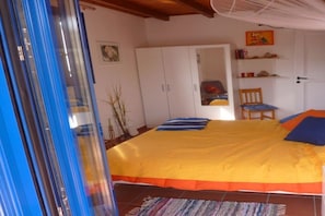 Ein Schlafzimmer mit einem Bett, einem Kleiderschrank, einem Sessel und einem Regal mit Büchern und Dekoration.