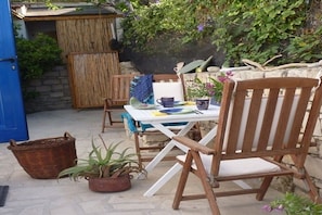 Eine Terrasse im Freien mit Tisch, Stühlen, einem Korbwägelchen und Blumentöpfen.
