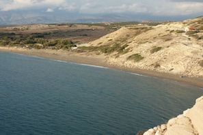 Eine Küstenlandschaft mit Strand, felsigem Gelände und einem kleinen Gebäude.
