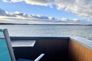 Une vue prise depuis un bateau doté d’un pont en bois et d’une rambarde en métal, donnant sur une étendue d’eau calme et une côte lointaine.