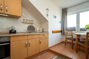A kitchen with wooden cabinets, a sink, a stove, and a dining area with a table and chairs. - House on the lake shore (Waren)